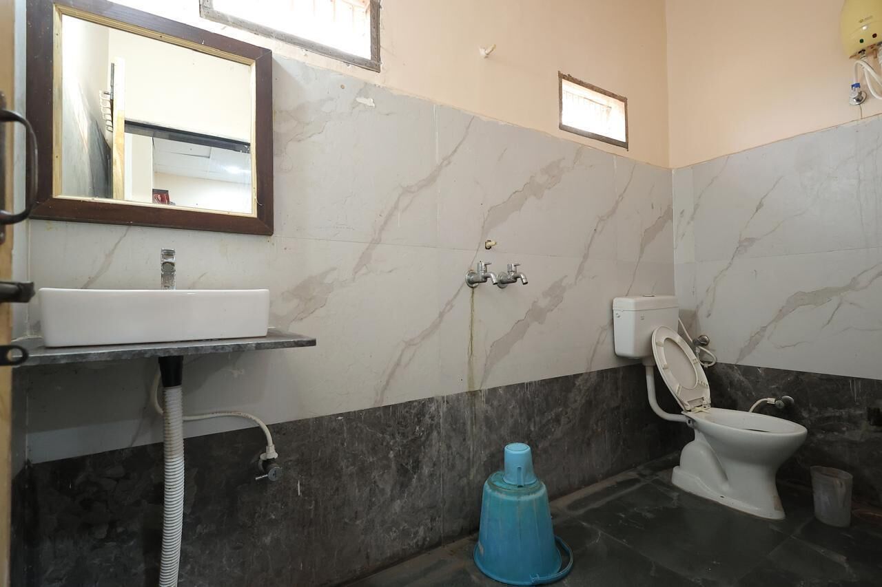 A bathroom with a sink, mirror, toilet, and a blue cleaning bucket.