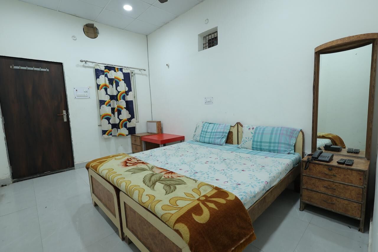 A bedroom with a bed, a wooden dresser, a mirror, and a door.