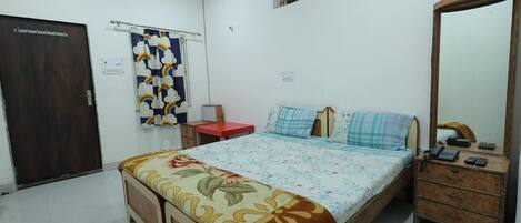 A bedroom with a bed, a wooden dresser, a mirror, and a door.