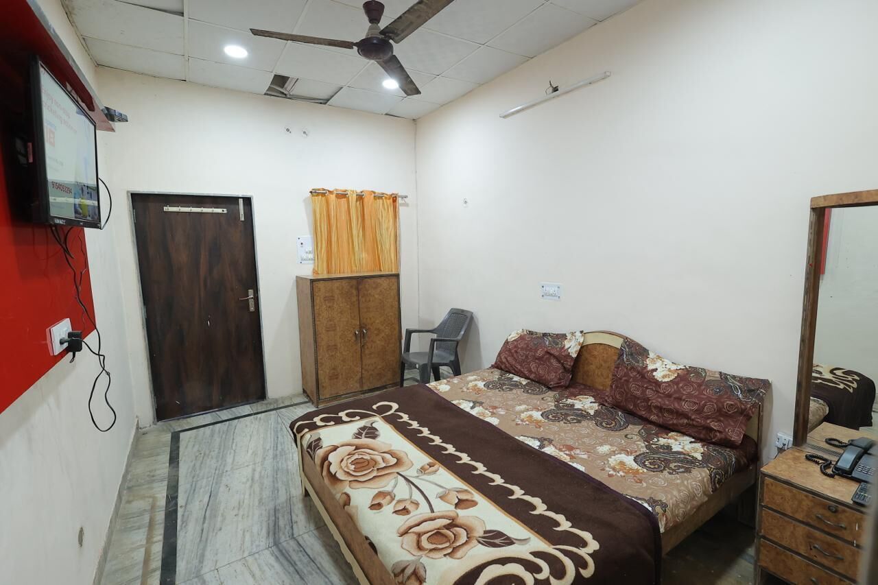 A bedroom with a bed, a wardrobe, a desk, a chair, a ceiling fan, and a television mounted on the wall.