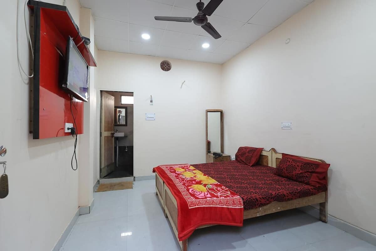 A bedroom with a bed, a ceiling fan, a TV mounted on the wall, and a door leading to a bathroom.