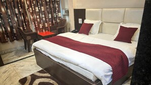 Quarto de hotel com uma cama grande, edredom vermelho e branco, piso de mármore e uma cadeira de madeira.
