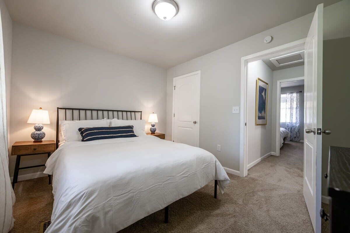 Une chambre à coucher avec un lit, des tables de chevet, une porte et un couloir.