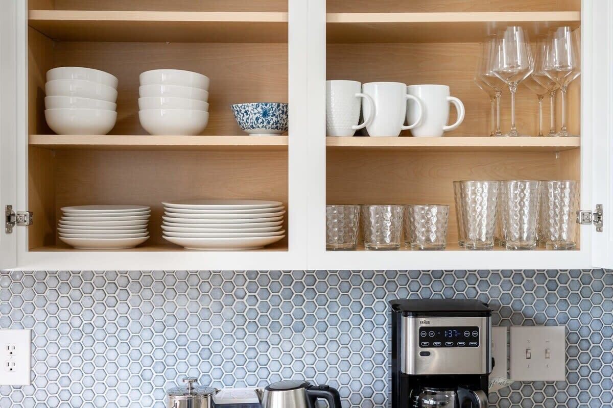A kitchen with wooden shelves holding white bowls, plates, and glassware.