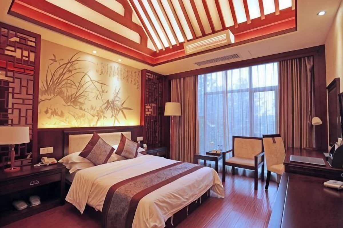 A hotel room with a large bed, a desk, a chair, a nightstand, and a wall with a decorative painting.