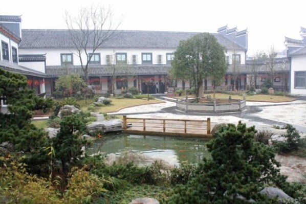 Une cour traditionnelle avec un bassin, un pont en bois et des bâtiments aux toits couverts de tuiles.