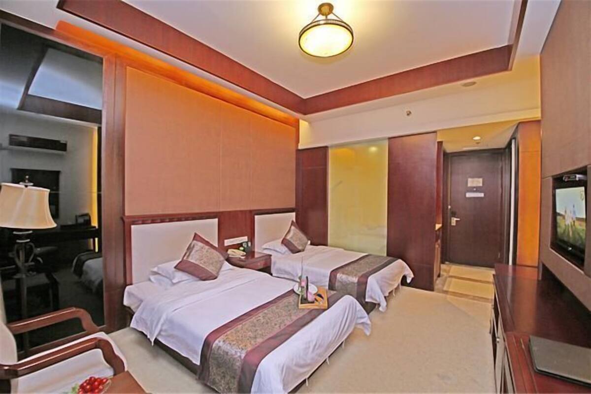 A hotel room with two beds, a desk, a chair, a television, and a door.