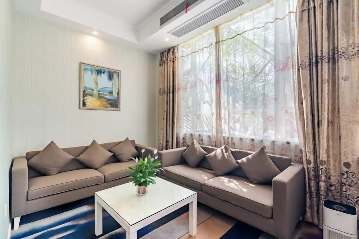 A living room with a sofa set, a coffee table, a painting on the wall, and a window with curtains.