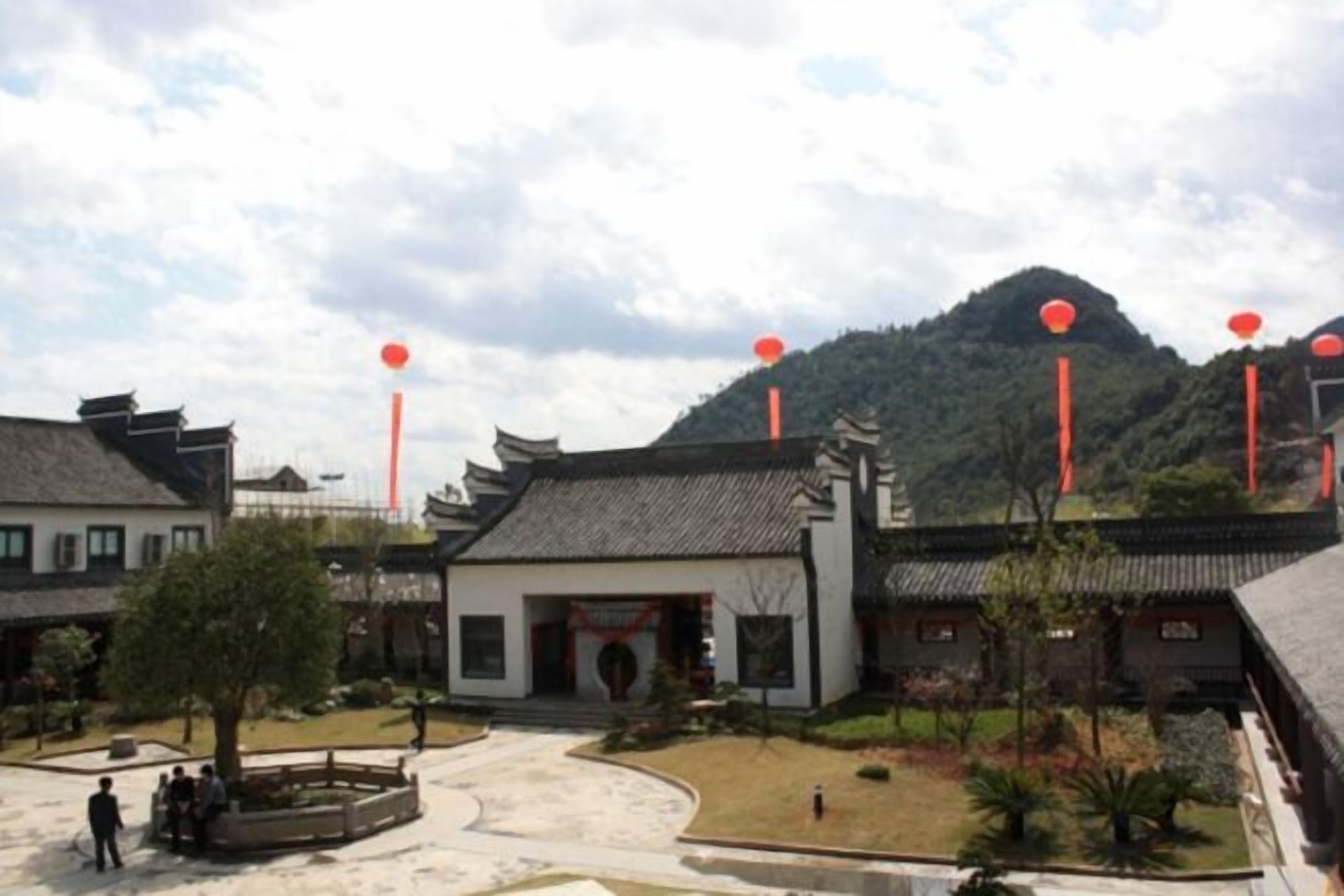 A traditional courtyard with buildings, a central tree, and a mountain in the background.