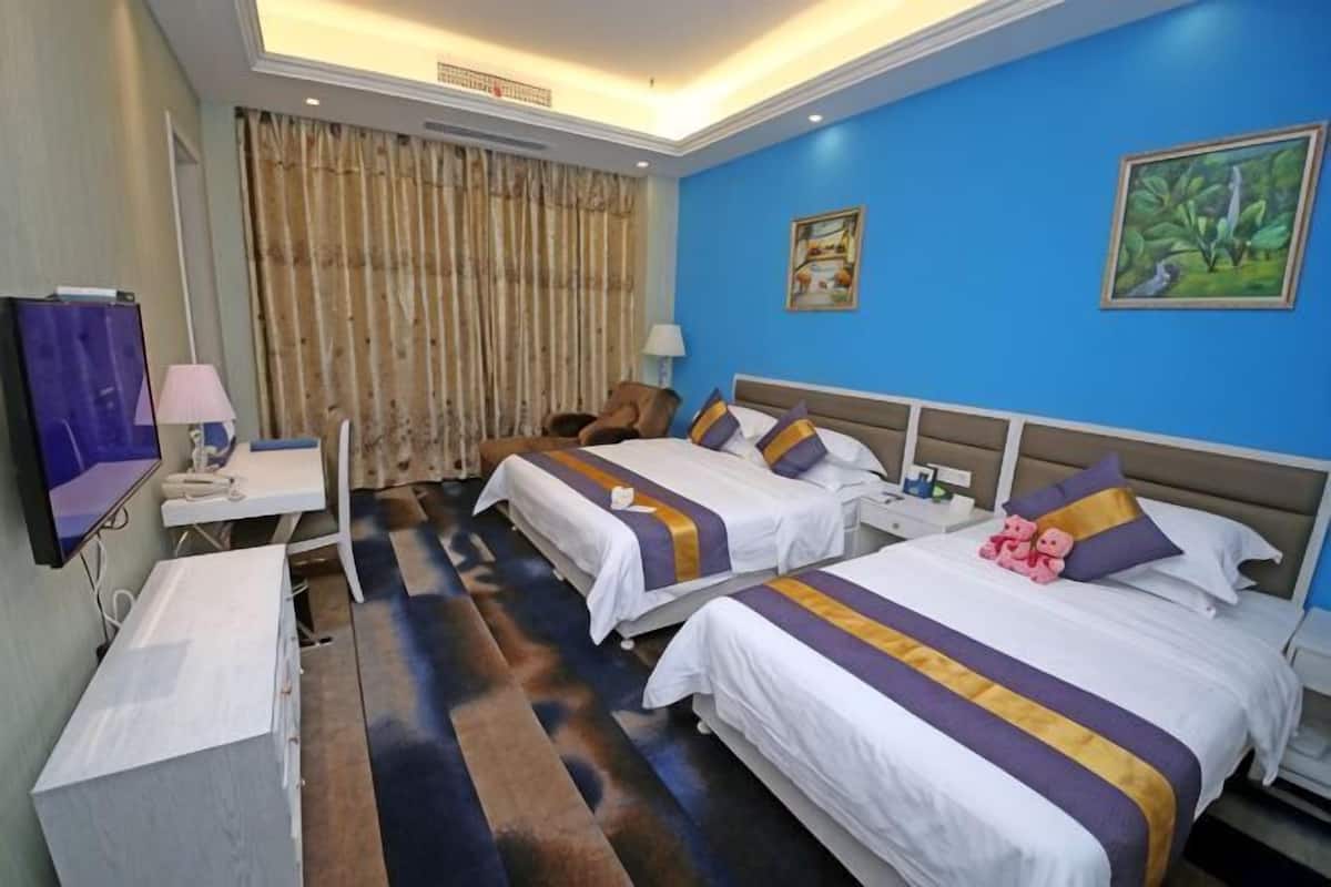 A hotel room with two beds, a desk, a chair, a TV, and a window with curtains.