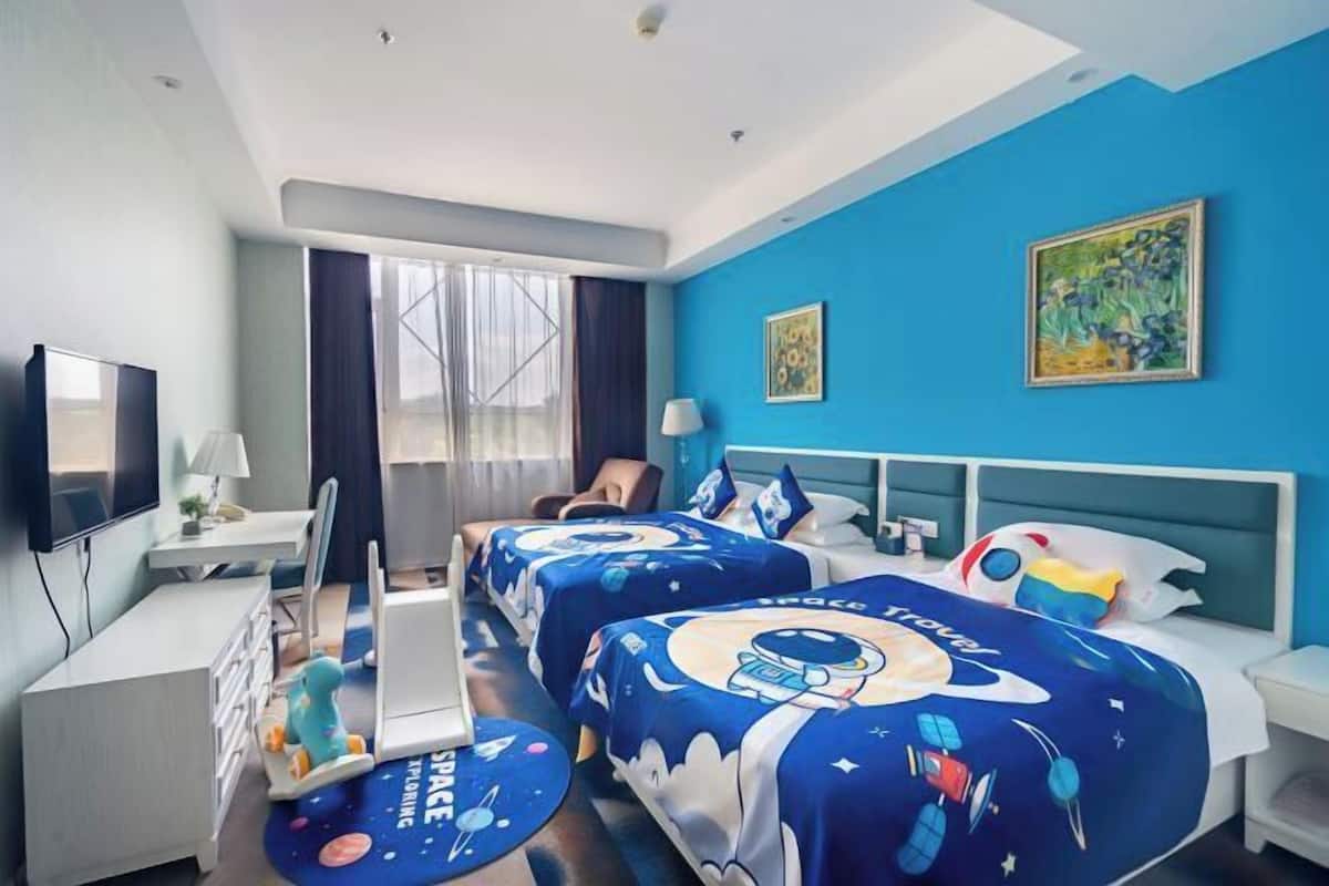 A hotel room with two beds, a desk, a TV, and a window with curtains.