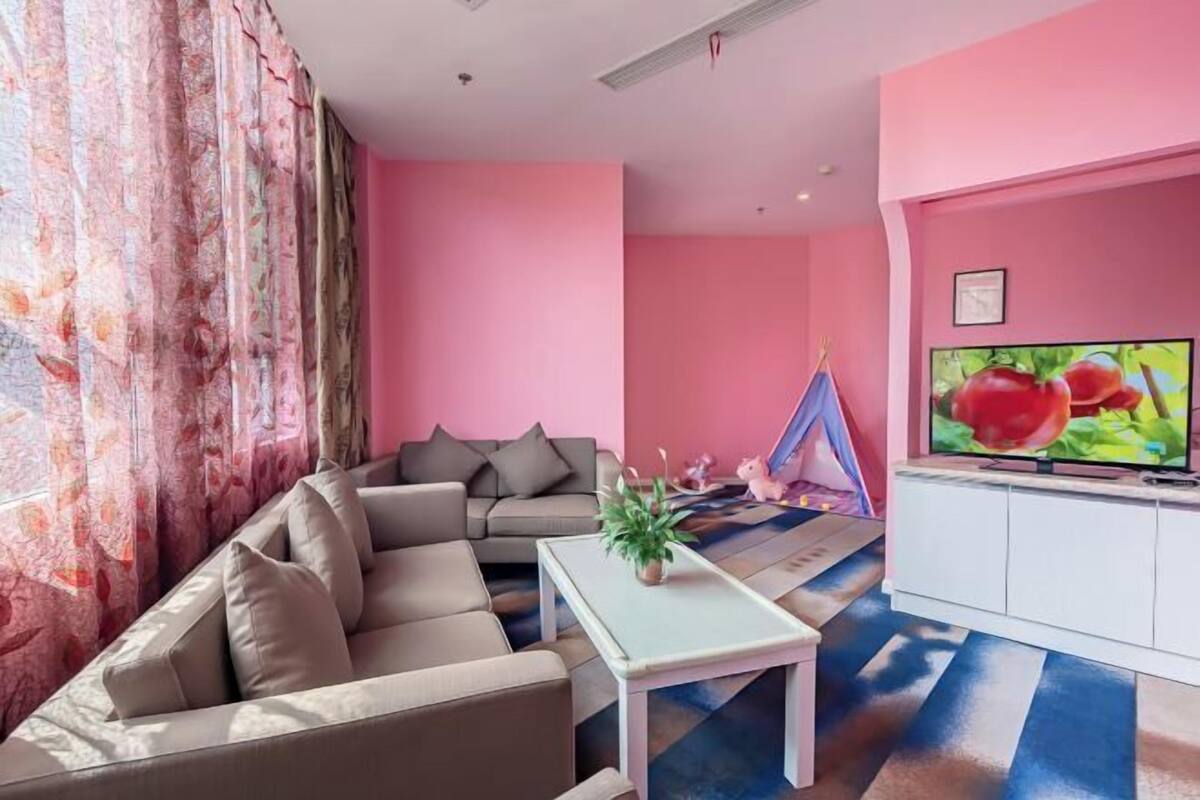 A living room with a sofa, a small table, a TV, and a pink wall.
