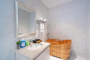 A bathroom with a marble wall, a sink with toiletries, a wooden bath tub, and a mirror. - Qinshuiwan Holiday Hotel (Ninghai Wujia Manor) (Ninghai)