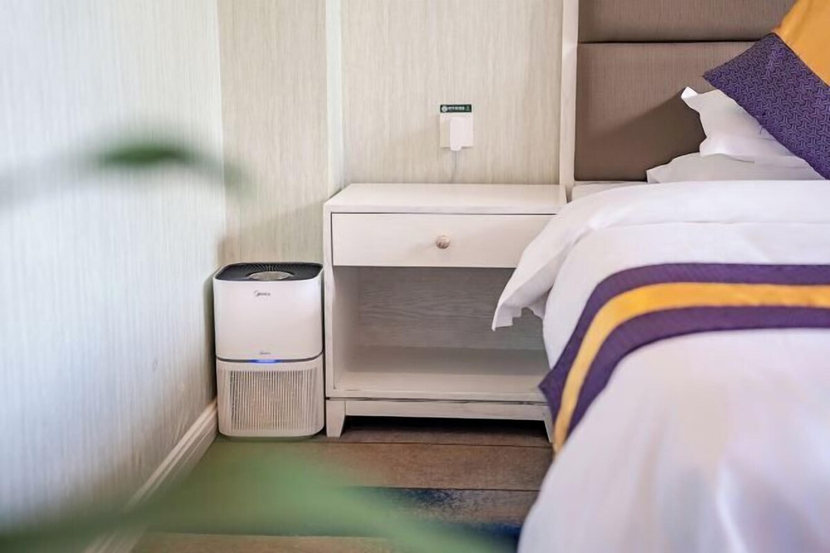 A hotel room with a bed, a bedside table, and a wall-mounted air purifier.