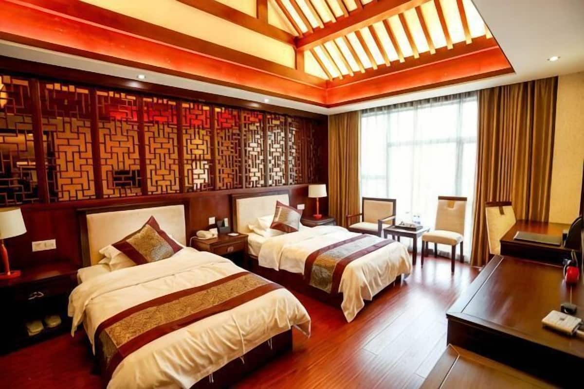 A hotel room with two beds, a desk, a chair, and a large window.