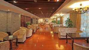 A hotel lobby with a long reception desk, multiple seating areas, and a brick wall. - Qinshuiwan Holiday Hotel (Ninghai Wujia Manor) (Ninghai)