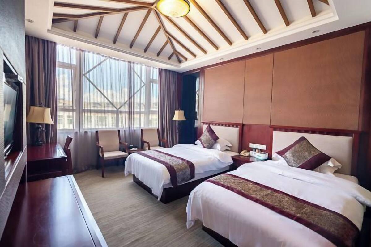 A hotel room with two beds, a TV, a desk, and a chair.