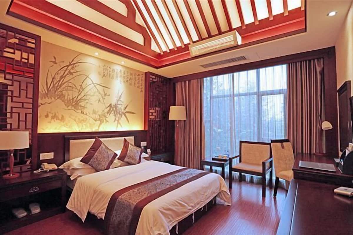 A hotel room with a large bed, a desk, a chair, a nightstand, and a wall with a decorative panel.