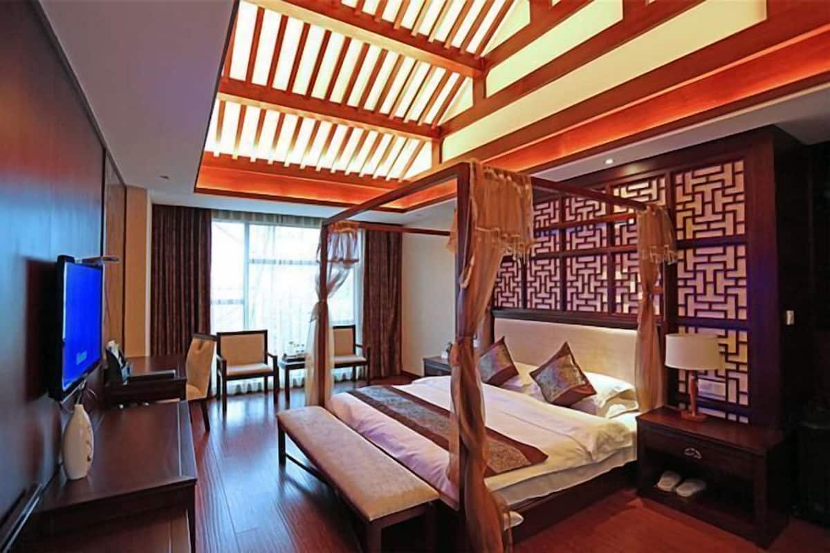 A four-poster bed with a canopy, a television, a desk, and a chair in a hotel room.