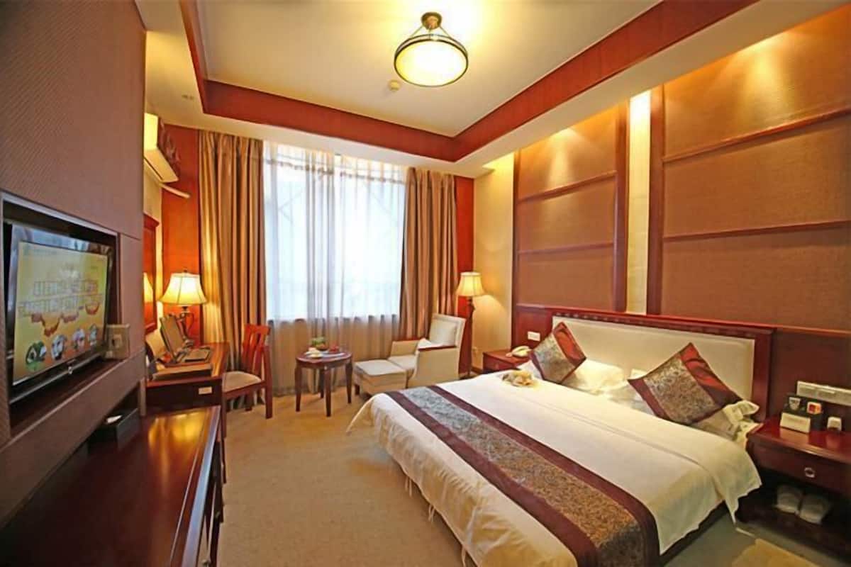 A hotel room with a large bed, a desk with a television, a chair, and a small table.