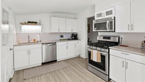 Una cucina moderna con pensili bianchi, lavastoviglie in acciaio inox, un fornello e un forno a microonde.