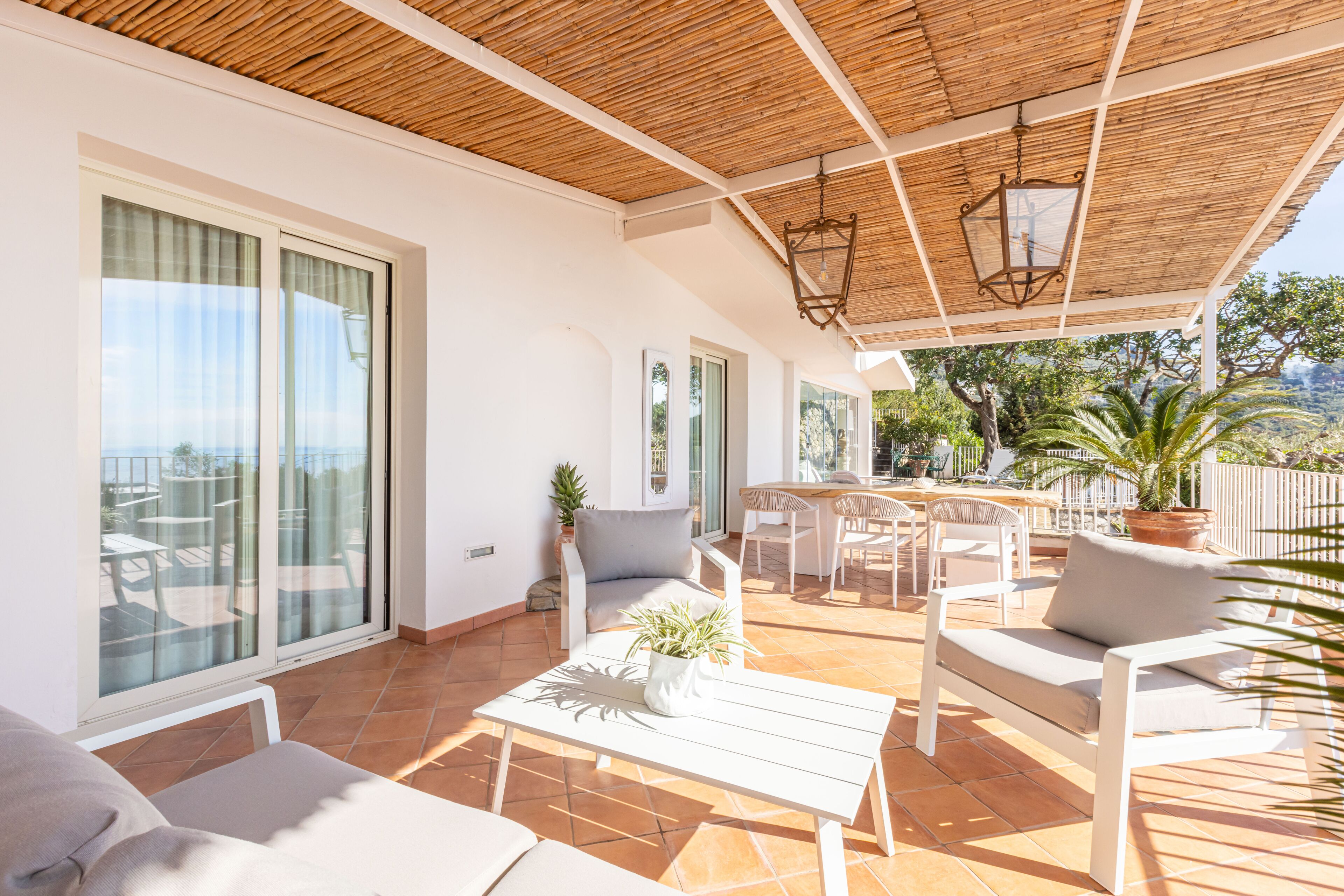A sunlit patio with white furniture, a table, and a potted plant.
