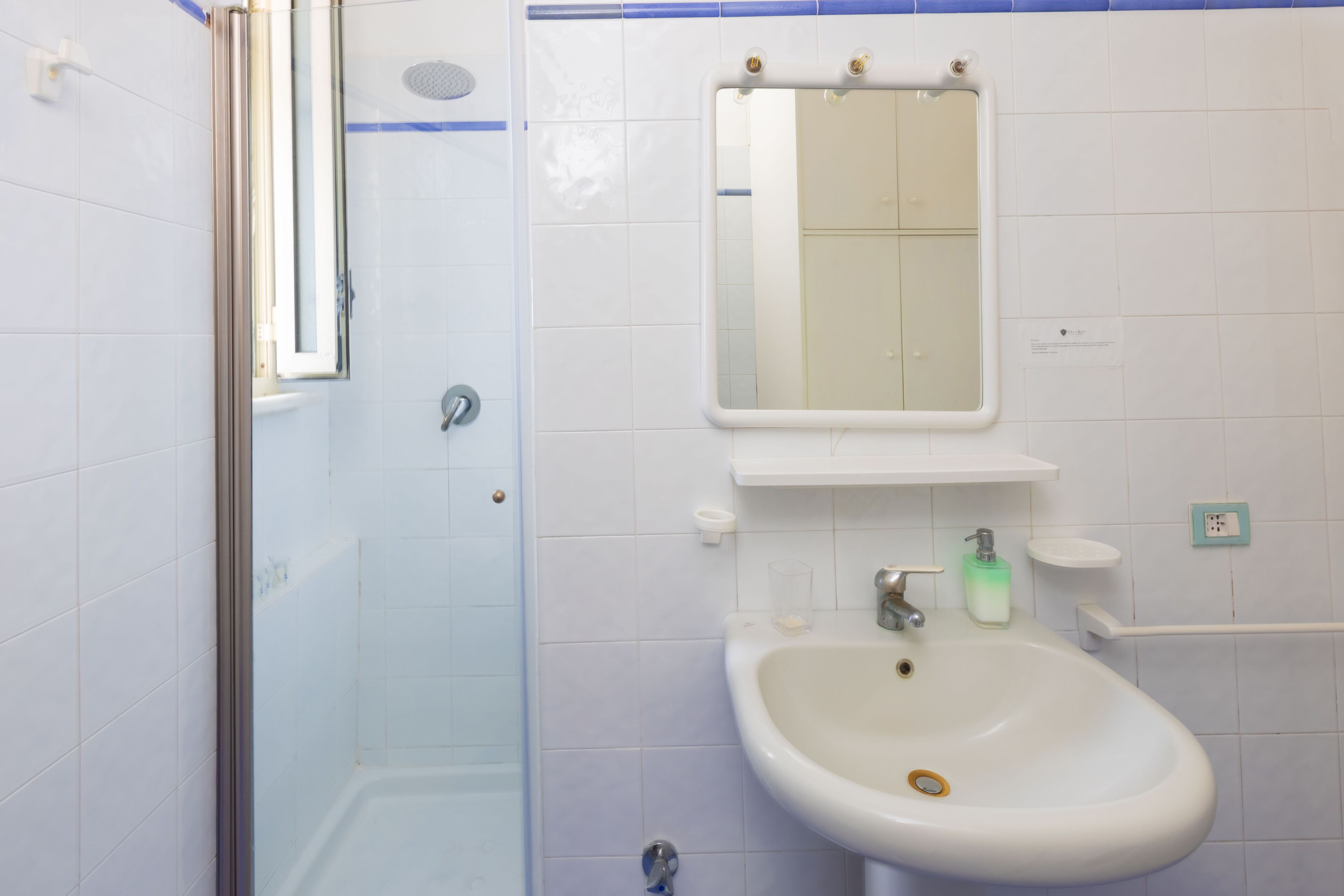 A bathroom with a glass shower enclosure, a sink with a mirror above it, and a small shelf with toiletries.