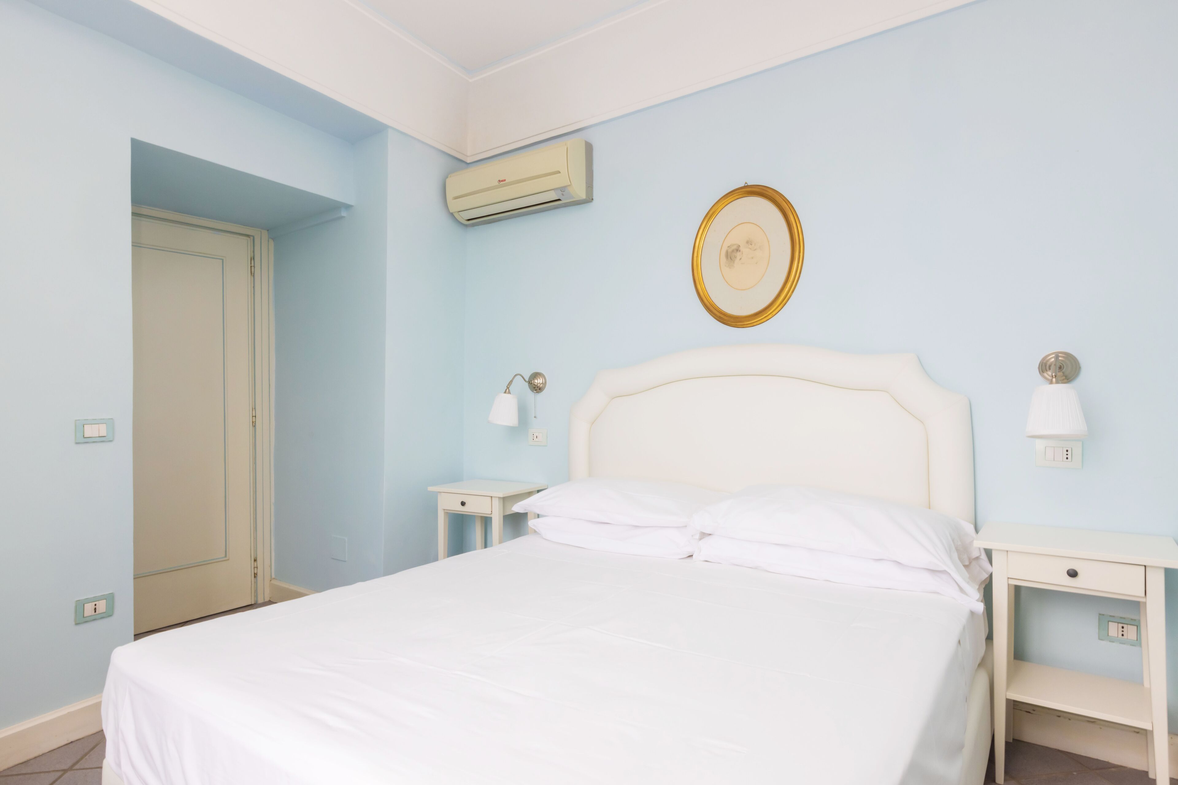 Een slaapkamer met een bed, nachtkastjes, een airconditioning en een wandlamp, plus een deur.