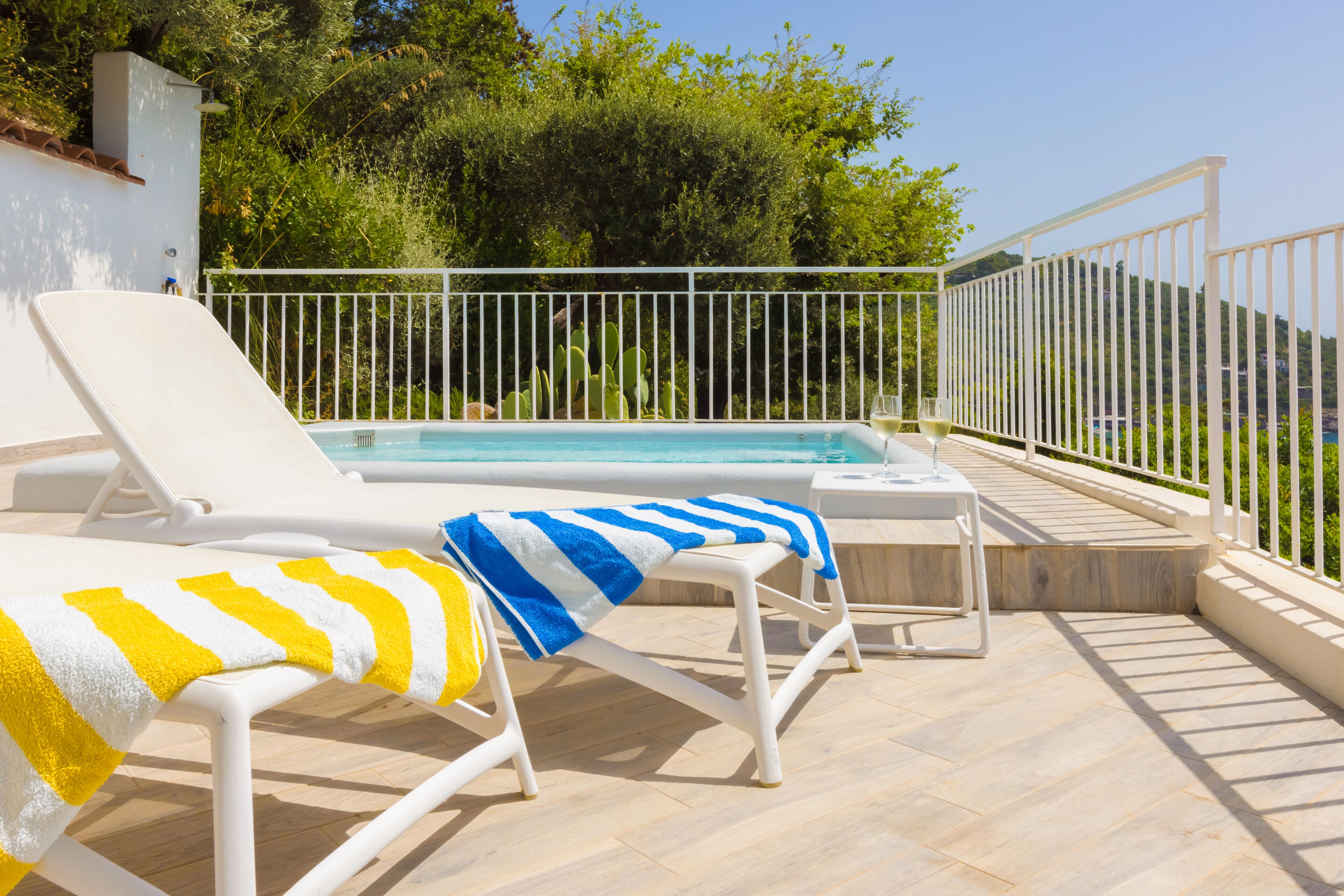A poolside area with two sun loungers, one with a yellow and white striped towel and the other with a blue and white striped towel.