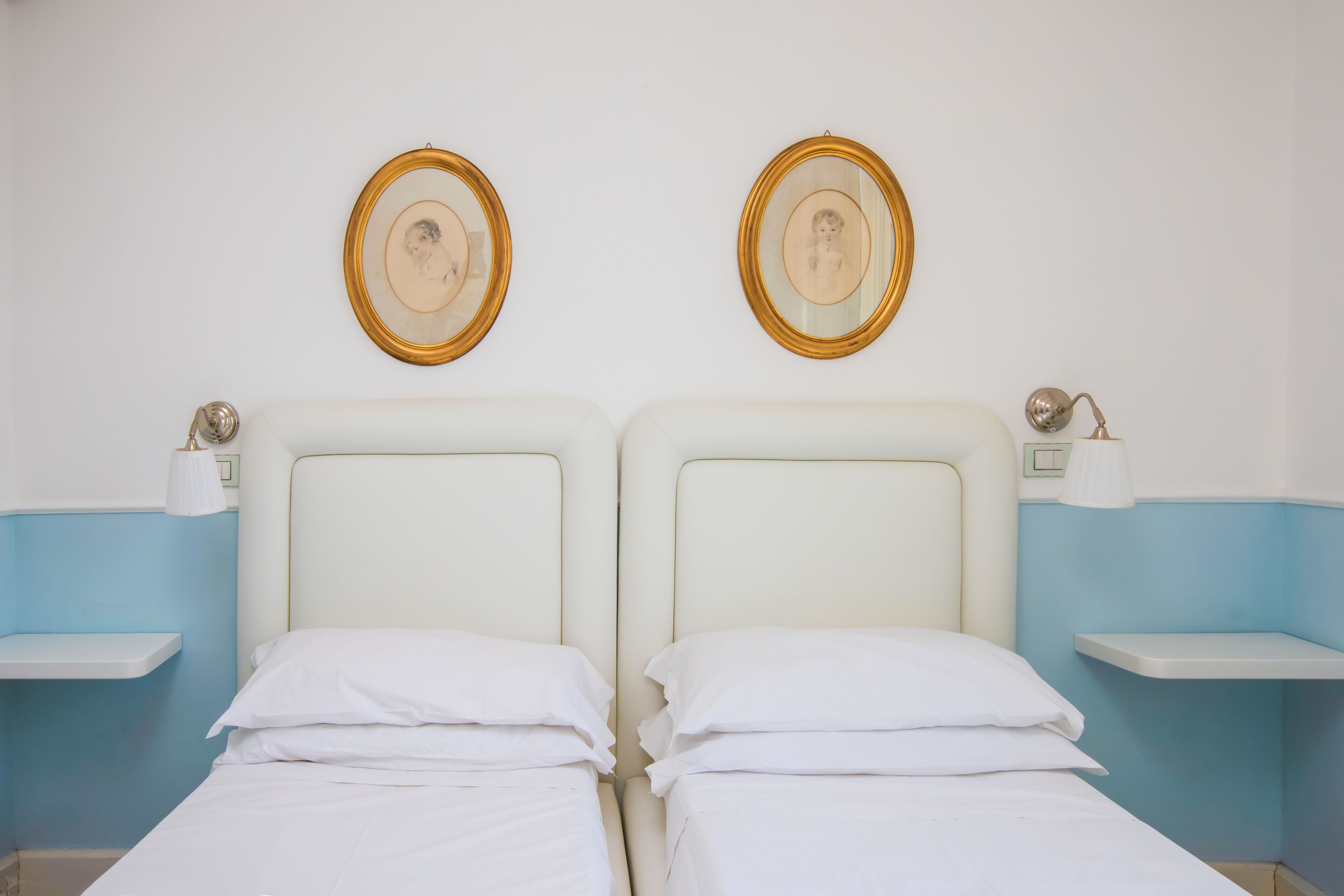 Habitación doble con dos camas, mesitas de noche, lámparas de pared y cuadros enmarcados.