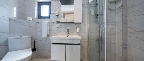 Uma casa de banho moderna com sanita, lavatório e chuveiro.