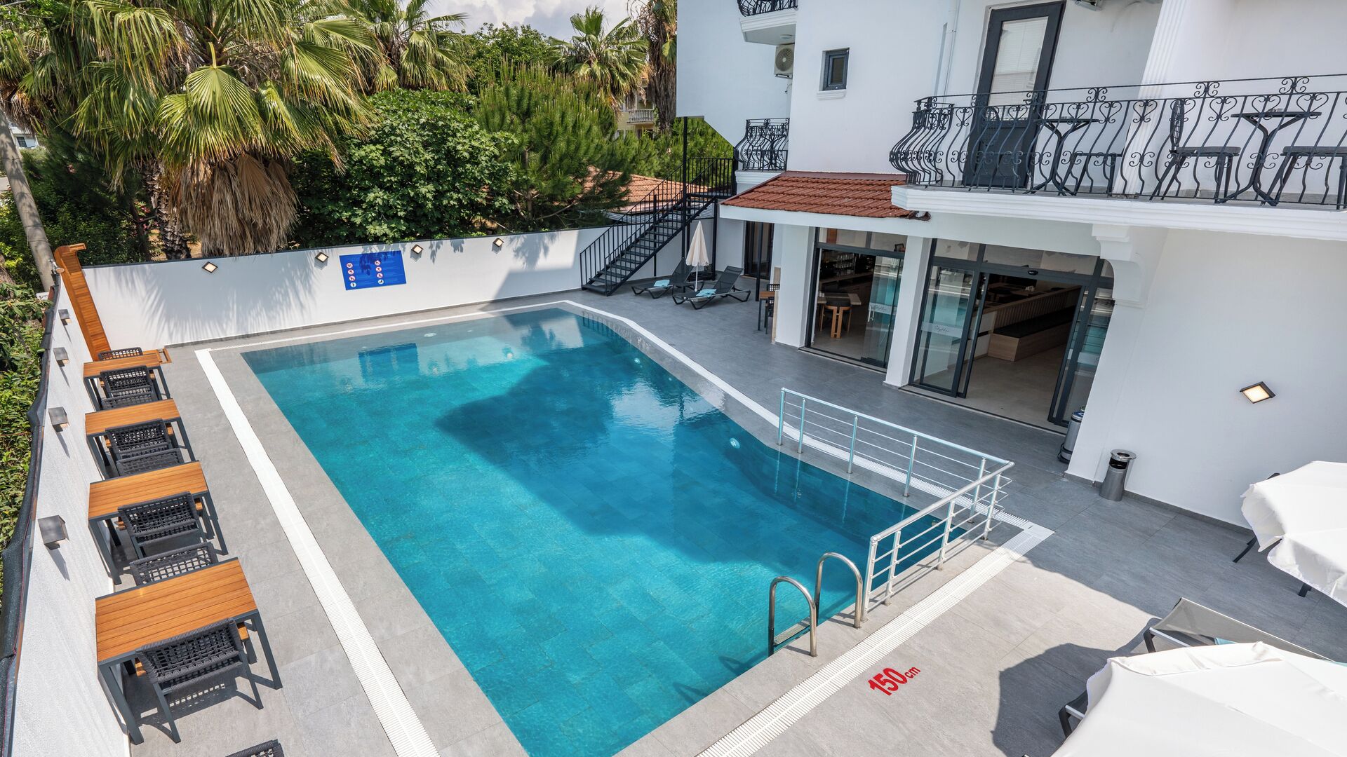 Una piscina con agua cristalina azul, rodeada de sillas de descanso y un edificio blanco con balcones.