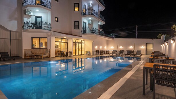 A swimming pool with lounge chairs and tables, a bar area, and a building with balconies. - Skykhan Otel (Fethiye)