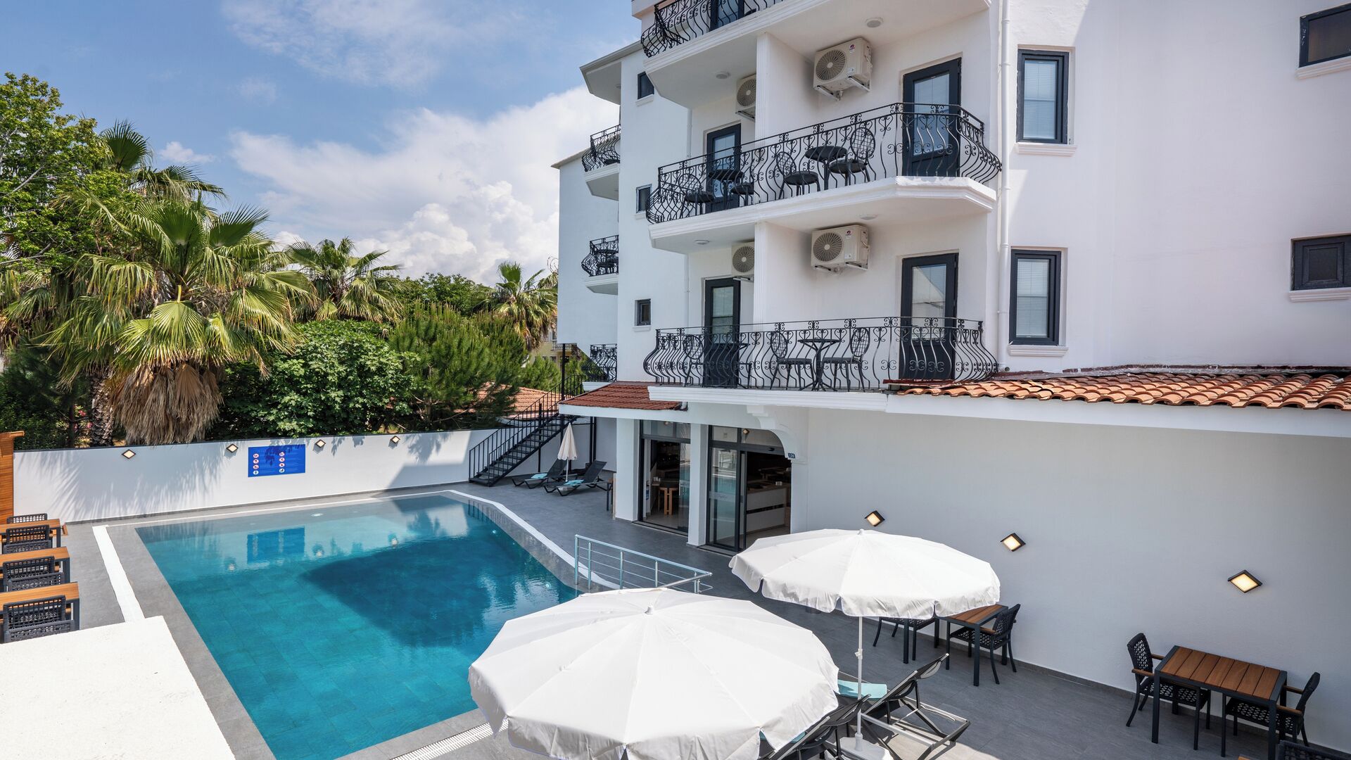 A hotel with a swimming pool, outdoor seating, and a white building with balconies.