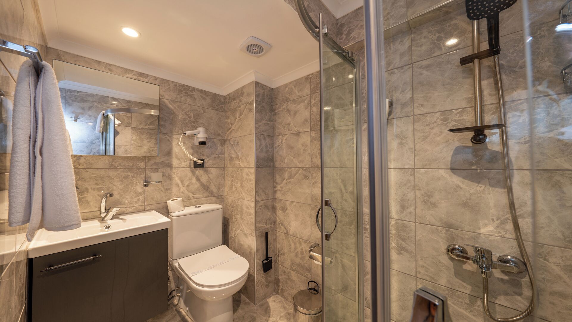 Une salle de bain moderne avec une douche à parois de verre, des toilettes, un lavabo avec un porte-serviettes et un miroir.