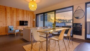 Un salon moderne comprenant un coin repas, des murs en bois, une grande fenêtre et un téléviseur à écran plat.