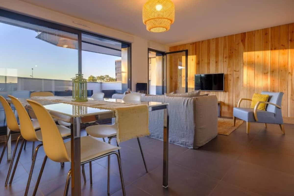 Un salon moderne comprenant un canapé, un téléviseur et un coin repas avec des chaises et une table.