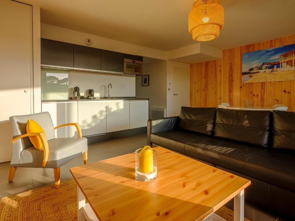 A modern living room with a wooden coffee table, a grey armchair, and a black leather sofa.