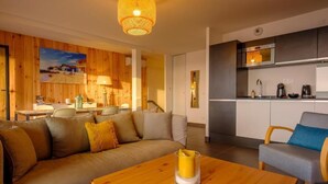 Un salon moderne avec un canapé en bois, une table basse et un coin cuisine équipé de placards et d’appareils électroménagers.