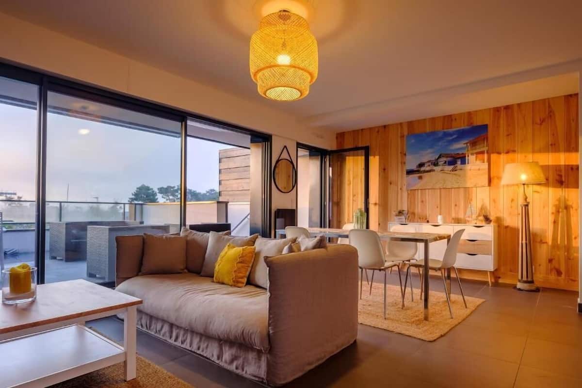 Un salon moderne avec un canapé, une table à manger et des chaises. Une grande fenêtre offre une vue sur la ville.