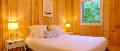 A wooden-paneled room with a bed, two bedside tables, and a window with a view of greenery.