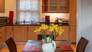 Un tavolo da pranzo con un vaso di fiori gialli, sedie di legno e sottopiatti rossi in una cucina con mobili in legno, un forno a microonde e un tostapane.