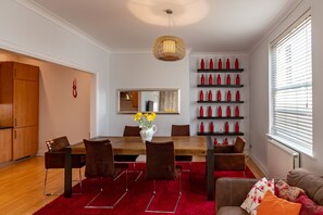 A modern dining area with a wooden table, brown chairs, and a red rug. There is a vase with yellow flowers on the table.