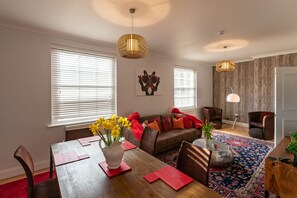 A modern living room with a wooden dining table, a brown sofa, and a patterned rug.
