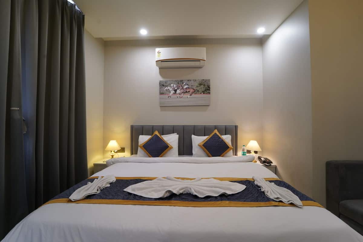 A hotel room with a bed, two bedside lamps, an air conditioner, and a painting on the wall.