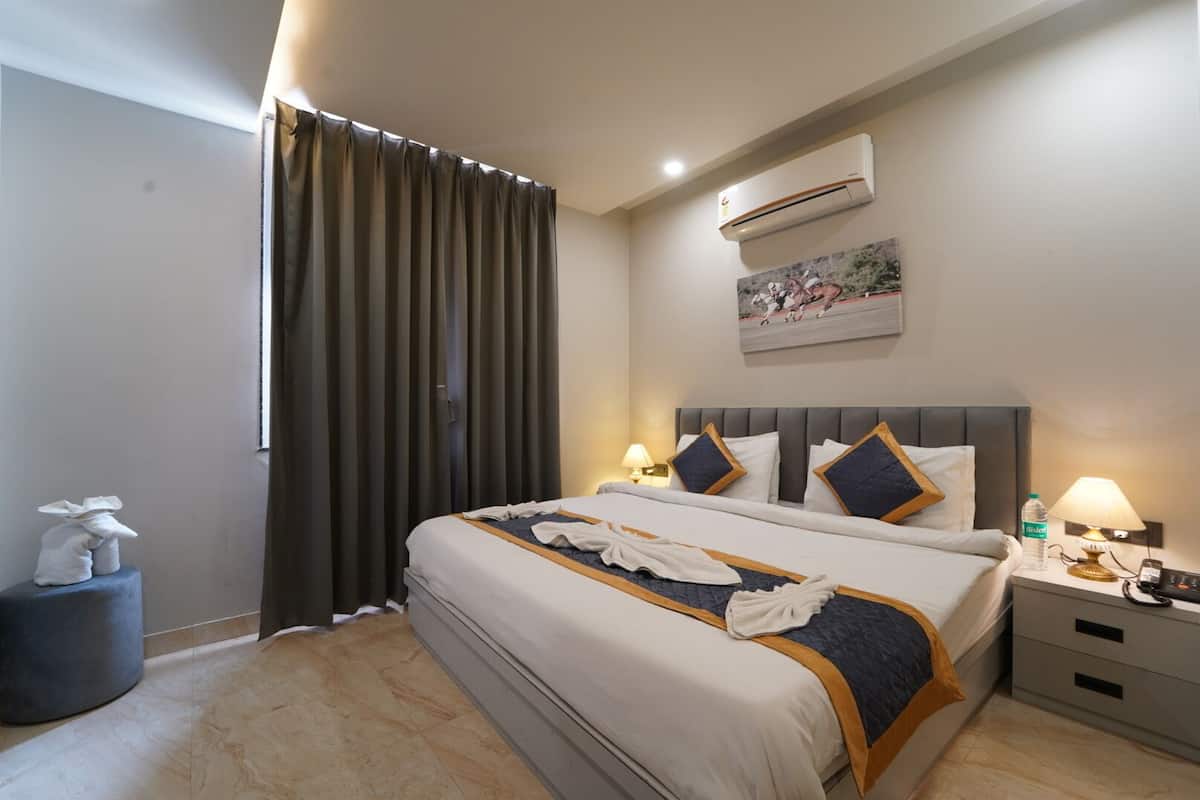 A hotel room with a bed, bedside tables, an air conditioning unit, a painting on the wall, and a window with curtains.