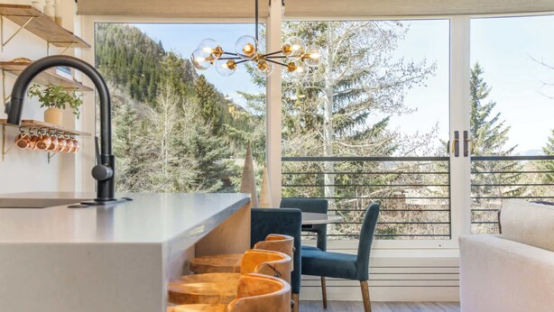A modern kitchen with a large window, a dining area with chairs, and a view of trees.