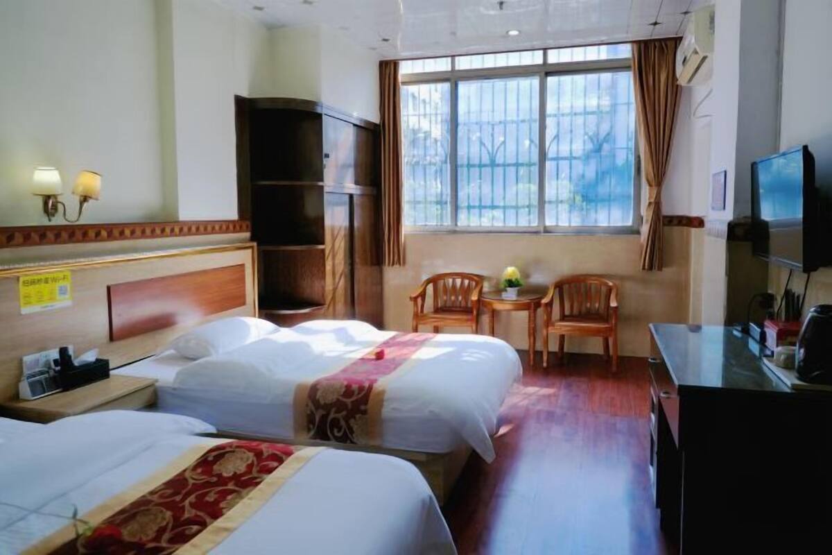 Habitación de hotel con dos camas, un escritorio, una silla, un televisor y una ventana con cortinas.