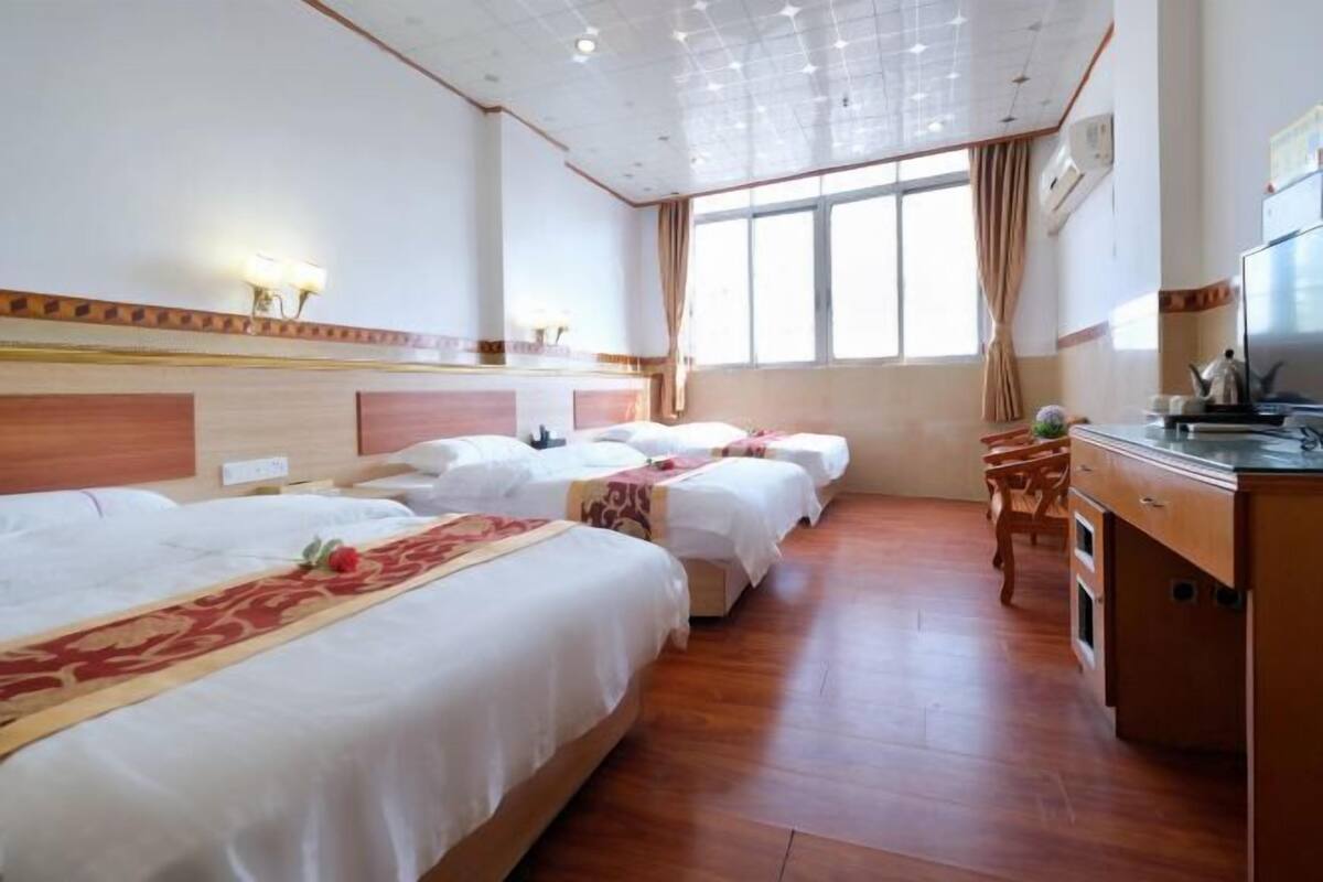 Habitación de hotel con tres camas, un aparador de madera, un escritorio y un ventanal grande.