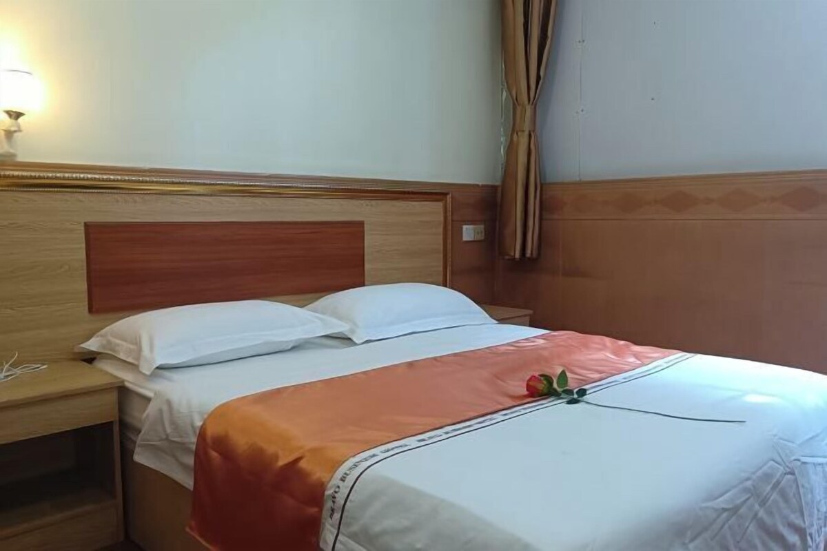 A hotel room with a wooden headboard, a single bed with white bedding, a nightstand, and a lamp.